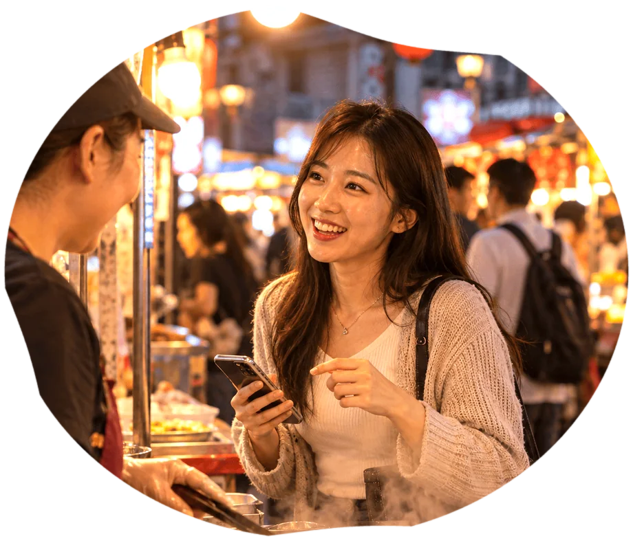 台湾の夜市の屋台で、スマホを持った女性が店員と笑顔で話している様子