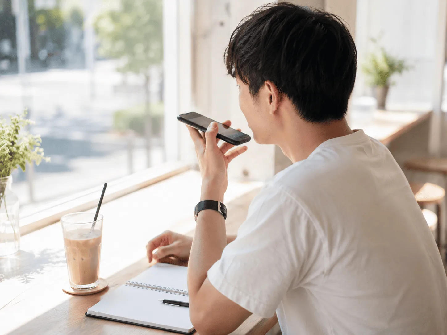 カフェの窓際でスマートフォンに向かって話している様子